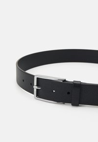 Ceinture en cuir noir avec une finition texturée, dotée d'une boucle en métal argenté et de plusieurs trous de réglage pour la fermeture.