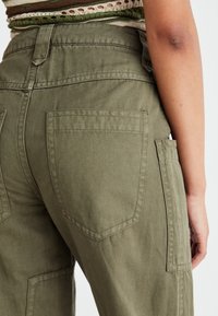 Pantalones cargo verde oliva con un corte relajado. Cuentan con dos bolsillos traseros y un bolsillo lateral, confeccionados en una suave tela de algodón texturizada.