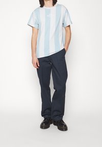 Světle modré a bílé pruhované tričko s kulatým výstřihem a krátkými rukávy, kombinované s námořnickými kalhotami a černými botami. Jednoduchý design.