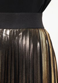 Svart och guld veckad kjol med svart elastisk midja och metallisk glans, med vertikala veck som kontrasterar mot den släta toppen.