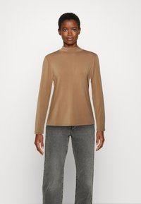 Blusa de mangas compridas e gola alta em castanho claro, feita de um tecido suave. Combinada com jeans de perna larga em cinza desbotado, criando um ajuste descontraído.