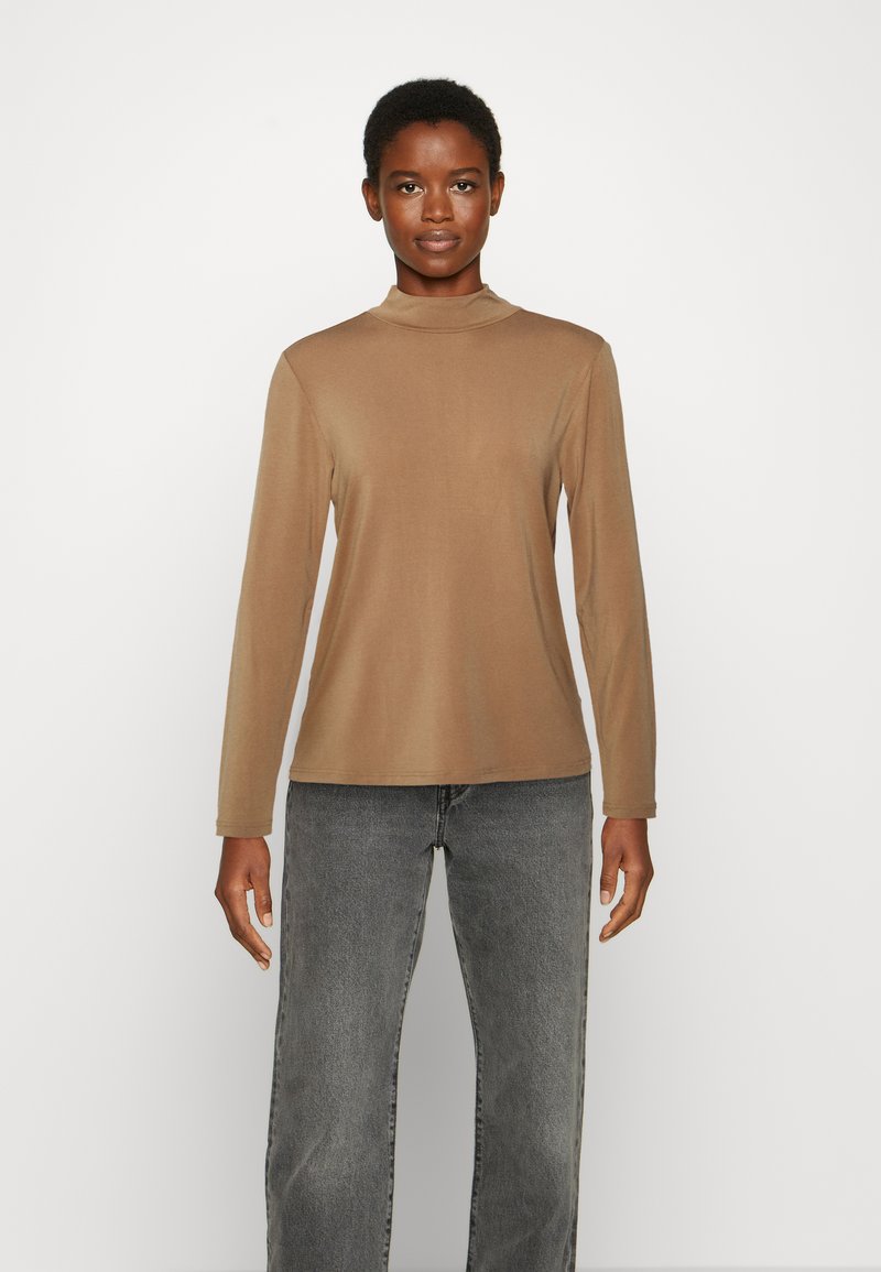 Blusa de mangas compridas e gola alta em castanho claro, feita de um tecido suave. Combinada com jeans de perna larga em cinza desbotado, criando um ajuste descontraído.