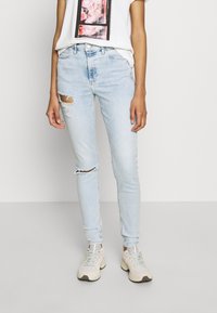 Jeans skinny de color azul claro con detalles de rasgados en las rodillas, combinados con una camiseta blanca con un gráfico floral rosa, y zapatillas ligeras.
