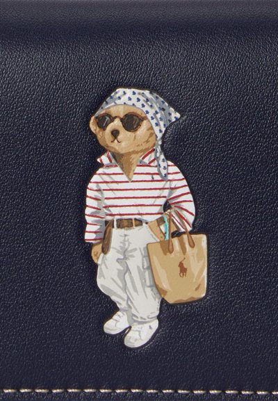 Αρκούδα που φοράει γυαλιά ηλίου, ριγέ πουκάμισο, λευκό παντελόνι, μαντήλι στο κεφάλι, κρατώντας μια καφέ τσάντα χειρός με λογότυπο αλόγου σε σκούρο υφασμάτινο φόντο.
