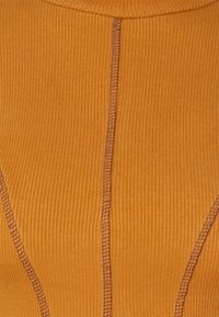 Ribbad tyg topp i varm orange, med strukturerad sömnad och figurnära design med tydliga linjer, som visar en sömlös konstruktion.