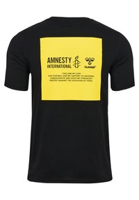 Czarna koszulka z dużym żółtym nadrukiem na plecach z tekstem i logo Amnesty International oraz Hummel.