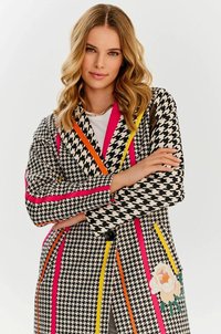 Płaszcz w czarno-białą szachownicę z jasnoróżowymi, żółtymi i pomarańczowymi paskami. Ozdobiony haftem kwiatowym oraz zapięciem na guziki.