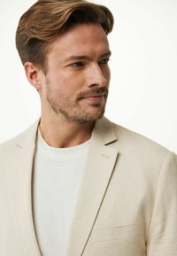 Mans beige linneblazer med texturerad yta och slagkrage, ihopparad med en vit t-shirt med rund nacke. Har en bröstficka.