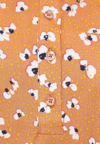Tessuto della camicia floreale pesca con piccoli fiori bianchi e dettagli blu, caratterizzato da bottoni rotondi di colore rosa e uno sfondo a pois.