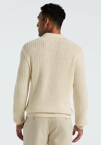 Cremfarbener Strickpullover mit einem strukturierten, offenen Maschendesign, geripptem Kragen, Bündchen und Saum. Die Rückansicht zeigt eine lockere Passform und minimale Nähte.
