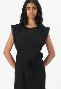 Black dress featuring a textured bodice with lace accents, short ruffled sleeves, and a waist tie for adjustable fit. Simple and elegant design.