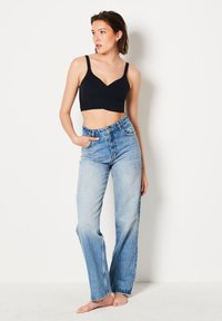 Bralette negro corto con tirantes anchos combinado con unos vaqueros de cintura alta de mezclilla azul claro. Los vaqueros tienen un corte relajado y un lavado desgastado.