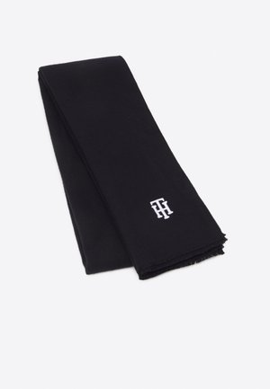 Zwarte, gevouwen sjaal met kleine witte geborduurde initialen "TH" nabij de rand op een effen lichte achtergrond.