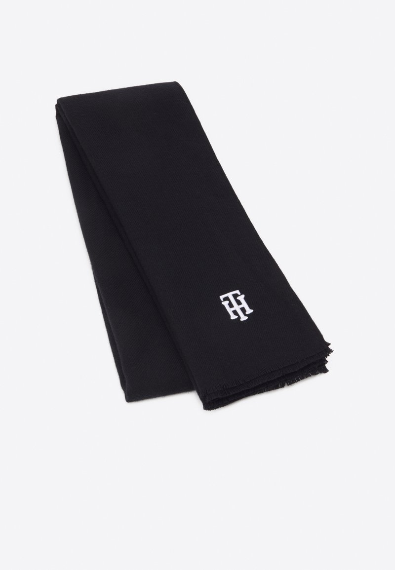 Écharpe noire pliée avec de petites initiales blanches brodées "TH" près du bord sur un fond clair uni.