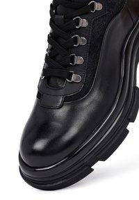 Bota de senderismo negra de cuero con paneles de tela texturada, ojales metálicos y una suela de goma duradera. Presenta un cierre de cordones y una puntera redondeada.