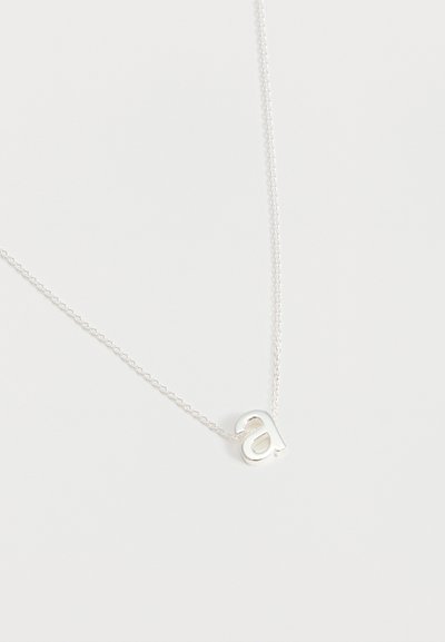 Collier délicat en chaîne d'argent avec un pendentif en forme de lettre minuscule "a" reposant sur un fond blanc uni.
