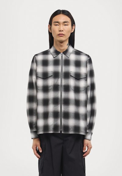Black and white checkered zip-up shirt with a collared neck, two chest pockets, smooth fabric, and long sleeves.