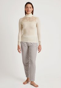 Lichtbeige top met kantdetail bij de halslijn en manchet, gecombineerd met gestreepte pyjamabroek in wit en grijs, met een scallopdesign.