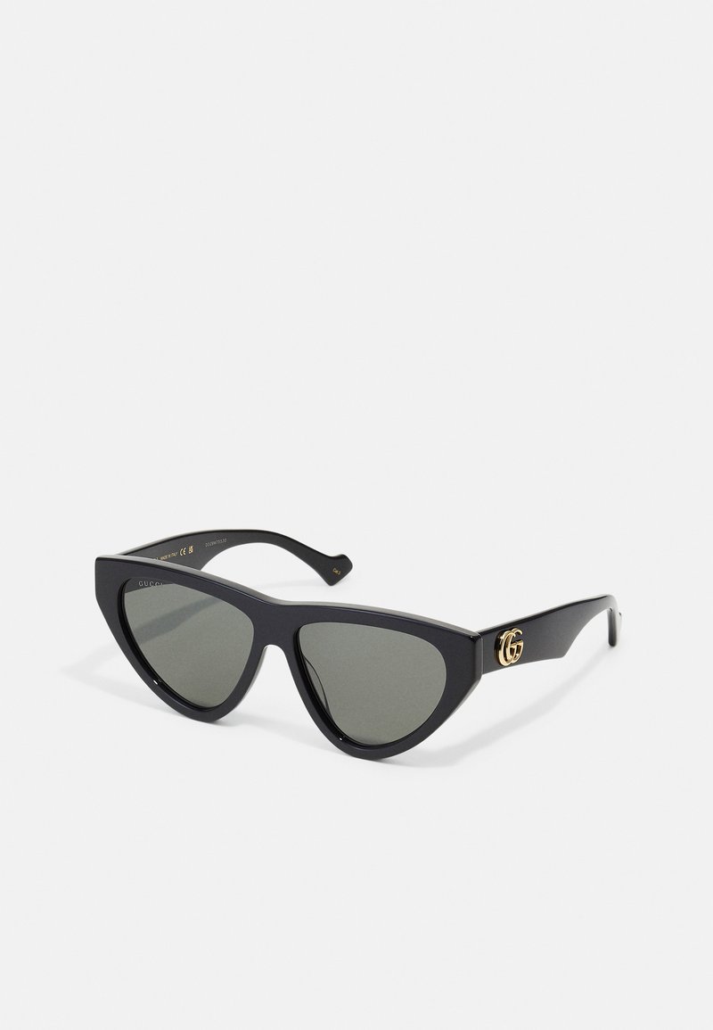 Black cat-eye sunglasses made of smooth plastic, featuring dark lenses and a gold logo accent on the temple.
