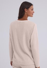 Beżowa bluza z miękkiego materiału, o luźnym kroju, z długimi rękawami i okrągłym dekoltem. Dyskretne przeszycia z tyłu.