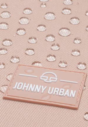 Krople wody na fakturowanej różowej tkaninie z przyszytą prostokątną metką z napisem "JOHNNY URBAN" białymi literami.