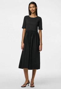 Crna haljina s kratkim rukavima, okruglim izrezom, strukirana u struku, lepršava suknja i glatka tekstura. Nositi s crnim sandalama.