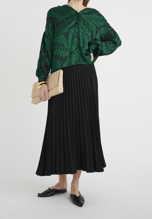 Grøn marmorbluse med knapper, parret med en sort plisseret maxiskirt. Tilbehør inkluderer en tekstureret beige clutch og sorte flade sko.