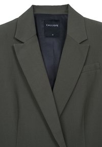 Blazer verde oliva realizzato in tessuto morbido, con revers a punta, taschino sul petto e fodera interna. Etichetta del brand visibile.