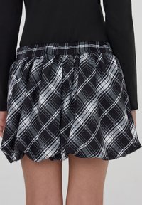 Gonna a scacchi nera, bianca e grigia con cintura arricciata indossata da una persona vestita con un top a maniche lunghe nero, vista da dietro.