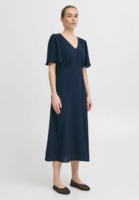 Navy blue midi dress with short puff sleeves, a v-neck, and textured dot pattern; paired with black flat shoes.