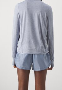 Světlé šedé tričko s dlouhým rukávem, volným střihem a postranním rozparkem, které je kombinováno s měkkými modrými šortkami s jednoduchým designem a pružným pasem.