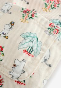 Mintás pamut szövet Moomin karakterekkel és virágos mintákkal, piros, zöld és sárga színekben, bézs háttéren; bordás textúra látható.