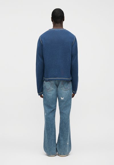 Μπλε πλεκτό πουλόβερ με κοντό σχέδιο, σε συνδυασμό με ανοιχτό μπλε τζιν καμπάνα με τσέπες στην πλάτη σε σχήμα καρδιάς και φθαρμένες λεπτομέρειες.