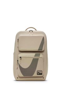 Beige rygsæk med mesh-paneler, dobbelte lynlåslommer, sort Nike-logo og robust håndtag. Glat stof med geometriske designelementer.