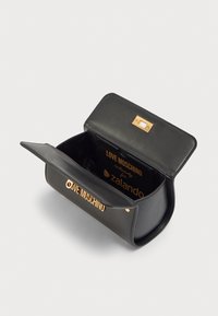 Μαύρη τσάντα χειρός από συνθετικό δέρμα με ορθογώνιο σχήμα. Χρυσά μεταλλικά στοιχεία με κούμπωμα και λογότυπο της μάρκας στο εσωτερικό. Ομαλή υφή.