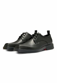 Scarpe di pelle nera con una trama liscia, punta arrotondata e cuciture discrete. Presentano una suola in gomma nera e un accento rosso sul tallone.
