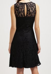 Robe en dentelle noire avec un corsage ajusté, un ourlet festonné et un dos à ouverture en forme de clé. Présente des motifs en spirale délicats sur l'ensemble.