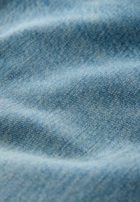 Gros plan sur un tissu en denim bleu clair montrant la texture et le motif de tissage avec des plis doux et des ombres.