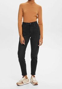 Zwarte jeans met een hoge taille en een slanke pasvorm, voorzien van riemlussen, gecombineerd met een bruine coltrui en beige sneakers met bruine accenten.