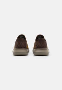 Braune und gelbe Slipper mit strukturierten Seitenpaneelen, einem glatten Rücken und einer geriffelten Sohle für besseren Halt.