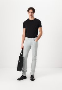 Tricou negru cu mânecă scurtă, pantaloni subțiri gri deschis, pantofi din piele negri. Ținând o geantă tote rectangulară neagră. Design minimalist.