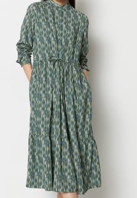 Abito a camicia verde con righe verticali in blu chiaro e beige. Presenta maniche lunghe, una cintura da annodare in vita e un orlo a più strati.