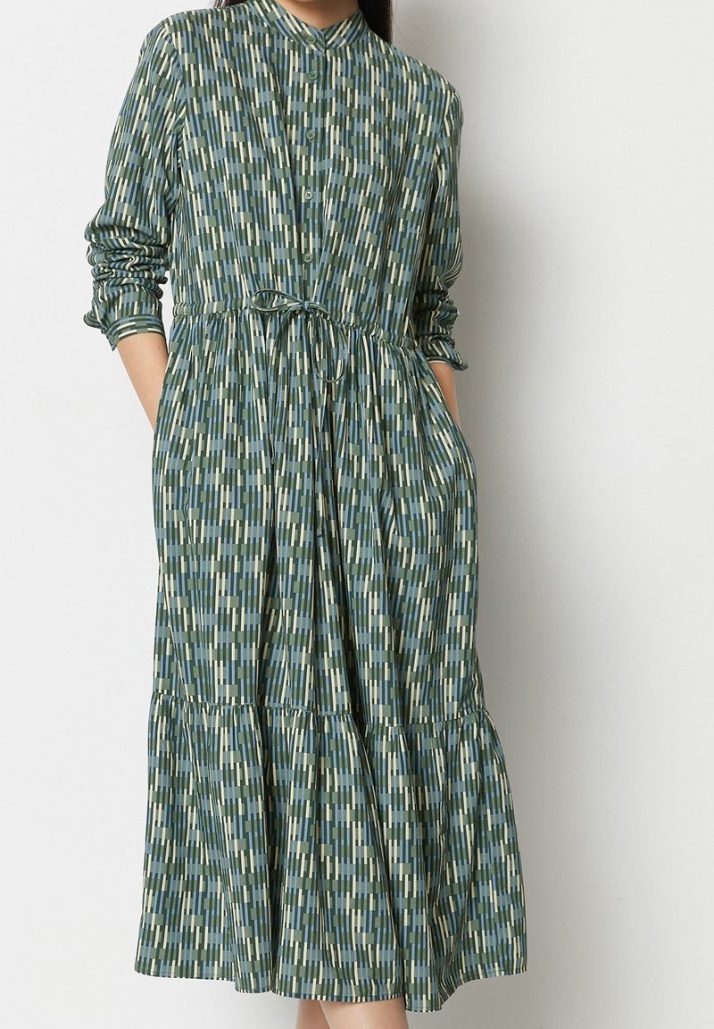 Abito a camicia verde con righe verticali in blu chiaro e beige. Presenta maniche lunghe, una cintura da annodare in vita e un orlo a più strati.