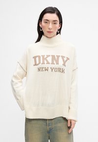 Maglione spesso in crema con alto collo, con la scritta "DKNY NEW YORK" lavorata a maglia beige. Polsini e orlo a coste con una vestibilità ampia. Design casual.