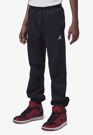 Underdel iført sorte sweatpants med hvid Jumpman-logo og rødsorte høje Nike Air Jordan sneakers på hvid baggrund.