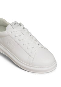 Fehér bőr sportcipő, lapos fűzős, kerek orrú, oldalán dombornyomott logóval. Simább textúrával és minimális varrással.