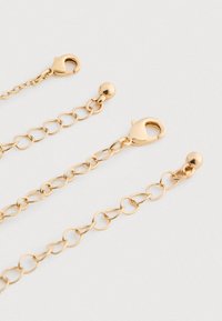 Tres extensoras de cadena de oro con cierres de langosta y enlaces de bola dispuestas sobre una superficie clara.