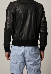Svart läderbomberjacka med ribbade stickade manschetter och midja, har en slät, något glansig yta och detaljer på axlarna.