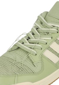 Světlé zelené tenisky s horním materiálem ze síťoviny a kůže, s texturovaným povrchem, kulatými tkaničkami a bílými pruhovanými akcenty.