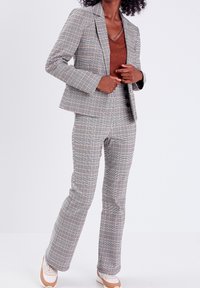 Grijs geruit pak met een getailleerde blazer met revers en hoge taille, flared broeken. Combinatie met casual sneakers.